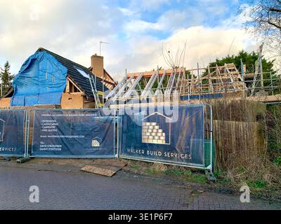 In einer Vorstadtstraße wird derzeit eine Wohnanlage renoviert, bei der ein Haus unter einer blauen Plane repariert wird und bei einem anderen freiliegendes Holz zu sehen ist Stockfoto