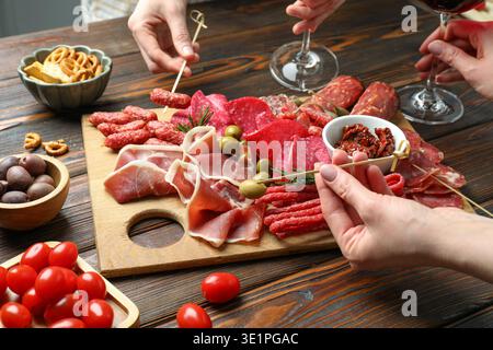 Die Leute essen leckere Snacks von der Wurstplatte am Holztisch, Nahaufnahme Stockfoto