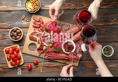 Die Leute essen leckere Snacks von der Wurstplatte an einem Holztisch, von oben aus Stockfoto