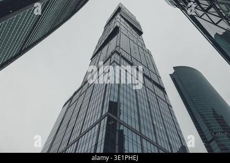 Eine dramatische, flache Perspektive, die direkt nach oben auf die hoch aufragenden Glas- und Stahlfassaden riesiger moderner Wolkenkratzer in einem geschäftigen geschäftsviertel blickt Stockfoto