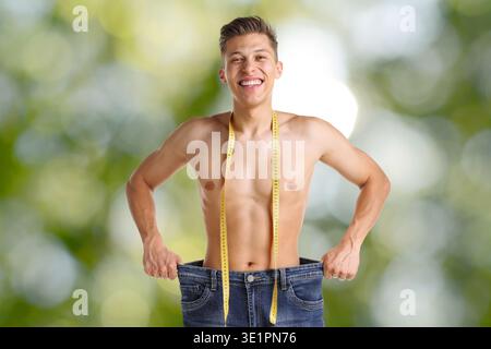 Glücklicher Mann in seiner alten Jeans vor verschwommenem grünem Hintergrund. Gewichtsverlust Stockfoto