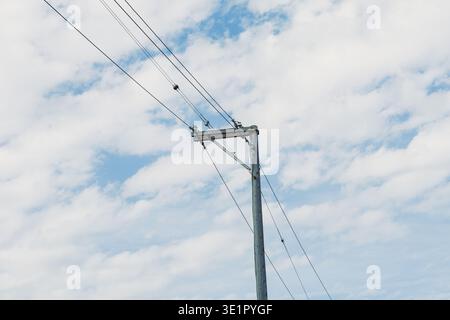 Hölzerne Versorgungsmasten führen Stromleitungen durch eine ländliche Landschaft unter einem Himmel voller Wolken und sonnendurchfluteter Bereiche tagsüber. Stockfoto