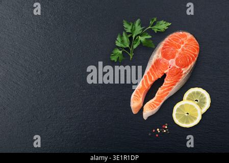 Frisches rotes Lachs-Fisch-Steak mit Petersilie und Zitrone auf schwarzem Schieferboden, Blick von oben Stockfoto