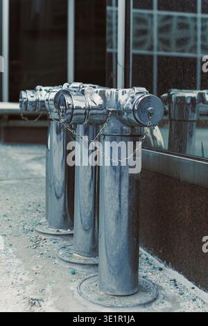 Auf einem Gehweg neben einem großen Gebäude mit Glasfenstern in einem städtischen Bereich befinden sich drei Metall-Hydranten. Stockfoto