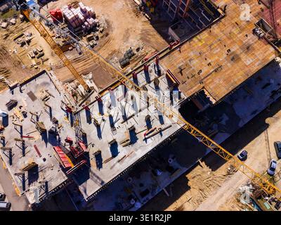 Arbeiter und Maschinen sind auf einer Baustelle anwesend, auf der ein neues Gebäude gebaut wird. Krane heben Materialien an und der Boden ist mit Klimaanlage beschäftigt Stockfoto