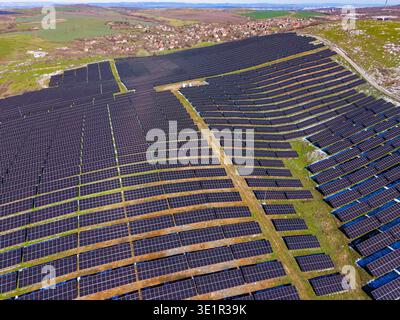 Reihen von Solarpaneelen werden auf freiem Land in einem ländlichen Gebiet unter klarem Himmel installiert. Die Panels sind in einem Raster angeordnet, in dem der effo für erneuerbare Energien dargestellt wird Stockfoto