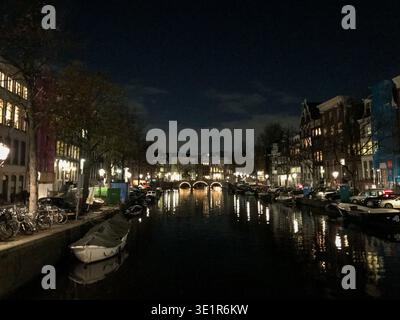Nächtlicher Blick auf die Kanäle in Amsterdam, mit traditionellen niederländischen Häusern, beleuchtet von warmen Lichtern, die auf dem ruhigen Wasser reflektieren. Romantisches Ambiente Stockfoto