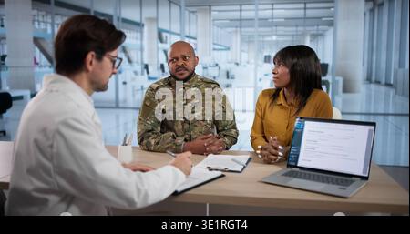 Ein afroamerikanischer Veteran spricht mit Arzt während der PTSD-Prüfung. Ein Mann in Militäruniform kommuniziert Stockfoto