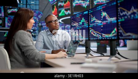 Junge Männer Und Frauen, Konzentriert Auf Bildschirme, Analysieren Börsentrends Während Der Handelszeiten Stockfoto