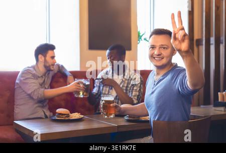 Aufgeregt, junger Kerl Bestellung mehr Bier, ruht mit Freunden an der Bar Stockfoto