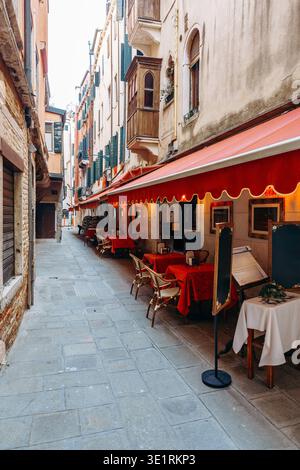 Ruhige Straße in Venedig mit leeren Tischen und Stühlen unter roten Markisen am Abend Stockfoto