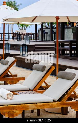 Luxuriöses Strandresort mit hölzernen Liegestühlen und weißen Sonnenschirmen. Stockfoto