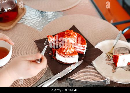 Rote Samtkuchenscheiben auf einem Tisch. Köstliches Dessert mit Frischkäse-Zuckerguss, Hand mit Gabel, Café-Einstellung, süße Köstlichkeiten, gehobenes Lifestyle-Essen Stockfoto