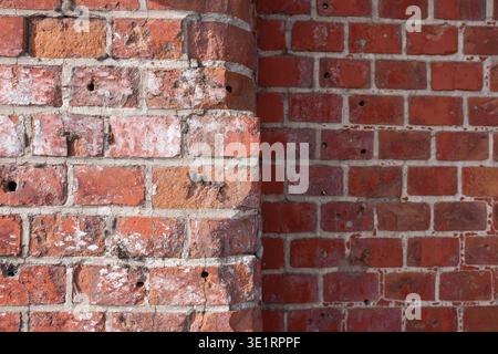 Nahaufnahme der strukturierten roten Ziegelwand mit Mörtelfugen und verwitterter Oberfläche, die architektonische Details und Mängel zeigt Stockfoto
