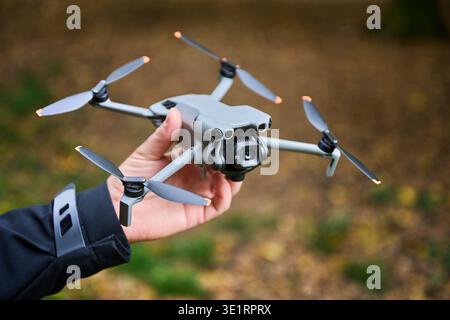 Eine Person hält eine schlanke Drohne in einem lebhaften Herbstpark. Die Umgebung ist mit bunten Blättern gefüllt, die die Schönheit der Natur zeigen, während sie sich auf den Start vorbereitet. Stockfoto