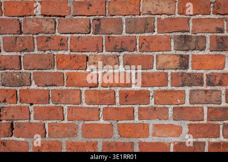 Rote Ziegelwand-Textur mit unterschiedlichen Farbtönen und Mörtelfugen, die ein rustikales und industrielles Erscheinungsbild für Hintergründe bieten Stockfoto