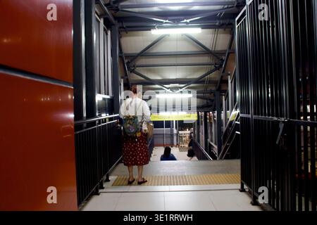 Eine Frau mit einem Rucksack steht nachts in einem schwach beleuchteten Transitweg, was auf Einsamkeit und Routinearbeiten hindeutet. Stockfoto