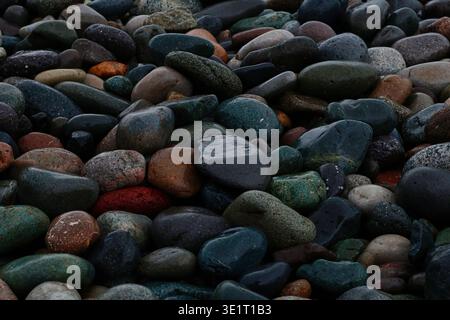 Ein professionelles Makrofoto eines mit Kieselsteinen bedeckten Ufers. Das Bild zeigt eine dichte Ansammlung von abgerundeten, wasserabgetragenen Steinen in verschiedenen Größen und Farbtönen Stockfoto
