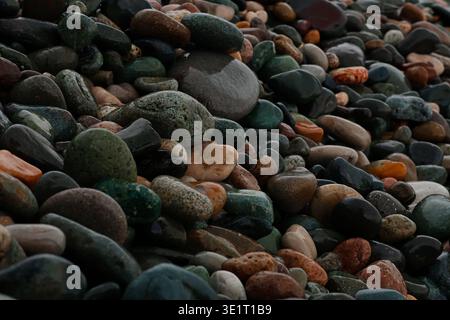 Ein professionelles Makrofoto eines mit Kieselsteinen bedeckten Ufers. Das Bild zeigt eine dichte Ansammlung von abgerundeten, wasserabgetragenen Steinen in verschiedenen Größen und Farbtönen Stockfoto