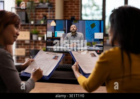 Die Personalabteilung bewertet Kandidaten während eines Online-Meetings, während der Geschäftsmann aus der Ferne mit seinem Team spricht. Der kaukasische Mann führt eine virtuelle Diskussion mit weiblichen Kollegen über Rekrutierungsstrategien. Stockfoto