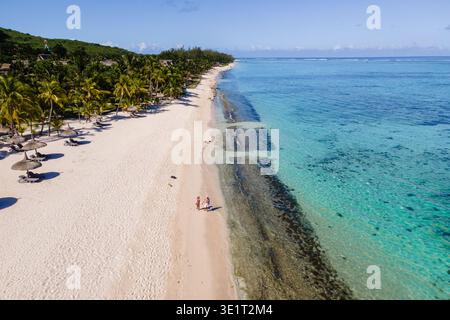 Ein Paar genießt einen ruhigen Spaziergang am unberührten Strand von Mauritius, umgeben von Palmen und atemberaubendem türkisfarbenem Wasser unter einem hellblauen Himmel. Ein paar Spaziergänge am Le Morne Beach auf Mauritius Stockfoto