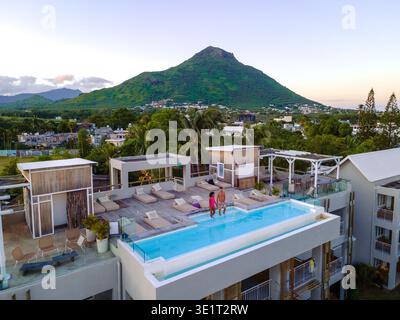 Entspannung trifft Schönheit in einem luxuriösen Pool in Rivire Noire, Mauritius. Ein Paar genießt einen ruhigen Moment, während die Sonne über den üppigen Bergen und dem pulsierenden Himmel untergeht und eine perfekte Urlaubsatmosphäre schafft. Stockfoto