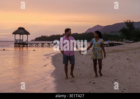 Ein paar Spaziergänge Hand in Hand am ruhigen Strand von Mauritius, umgeben von malerischer Landschaft und einem atemberaubenden Sonnenuntergang. Die warmen Farben schaffen eine traumhafte Atmosphäre für ihren romantischen Urlaub. Stockfoto
