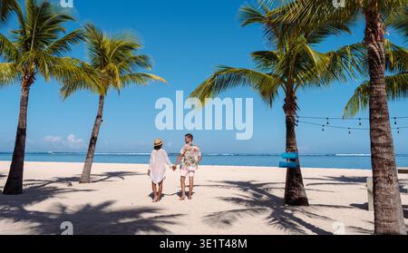 Das Paar genießt einen romantischen Spaziergang entlang der unberührten Küste von Mauritius, umgeben von üppigen Palmen und einem ruhigen Meer. Der hellblaue Himmel bildet die perfekte Kulisse für ihren Urlaub. Stockfoto
