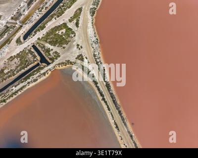 Aus der Vogelperspektive sehen Sie das Wasser mit markanten rosafarbenen Tönen und gedämpften Erdtönen, die durch einen dünnen Landstreifen getrennt sind, Aigues-Mortes, Occitanie, Frankreich. Stockfoto