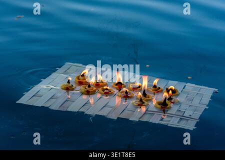 Ein kleines Holzfloß mit mehreren brennenden Öllampen schwimmt auf dem blauen Wasser des Pichola-Sees in Udaipur und hinterlässt eine leichte Rauchspur. Stockfoto