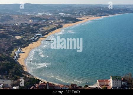 Aus der Vogelperspektive, wo der goldene Sand auf das endlose türkisfarbene Meer trifft, gesäumt von Gebäuden und fernen Hügeln, Istanbul, Türkei. Stockfoto