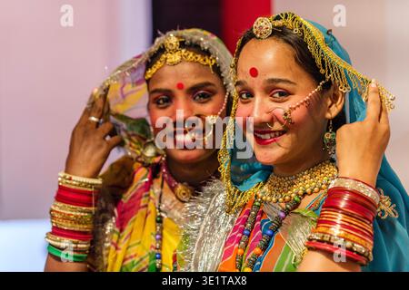 Zwei lächelnde junge Frauen in Udaipur tragen während eines Festivals farbenfrohe traditionelle Rajasthani-Kleidung mit kunstvollem Goldschmuck und lebendigen Dupatten. Stockfoto