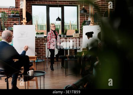 Ältere Frau professionelle Künstlerin unterrichtet Gruppe von Studenten neue Zeichentechniken in der Studioklasse, Menschen lernen zeichnen für persönliches Wachstum, besuchen kreative Workshops mit Familie und Freunden Stockfoto