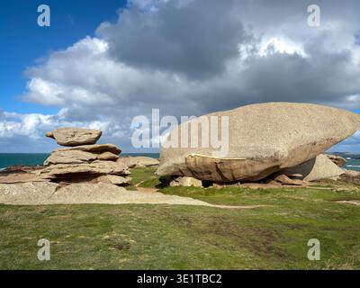 Ausgewogene Granitstapel stehen neben einem riesigen Felsbrocken in Tregastel an der Pink Granit Coast in der Bretagne Frankreich mit grasbewachsenem Boden und dramatischen Wolken o Stockfoto
