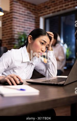 Stress und Ermüdung sind offensichtlich, da eine Geschäftsfrau bis spät in die Nacht in einem modernen Büro arbeitet und unter Druck ihre Arbeitsbelastung und ihre Aufgaben bewältigt. Karriere Burnout und Stressmanagement. Stockfoto