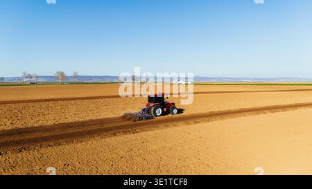 Aus der Vogelperspektive eines Traktors, der die reiche, braune Erde in starkem Kontrast zum klaren blauen Himmel bebaut, Sremska Mitrovica, Vojvodina, Serbien. Stockfoto