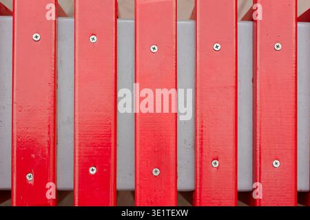 Draufsicht auf eine rote Holzbank oder einen Zaun mit silbernen Schrauben auf grauem Hintergrund. Abstrakte Textur von rot lackierten vertikalen Dielen mit Metallbolzen, Stockfoto