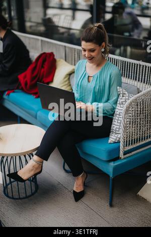 Zusammenarbeit im Unternehmen: Frau arbeitet an einem Laptop in einem Café im Freien, während sie lächelt und tippt Stockfoto