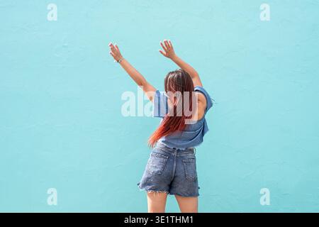 Attraktive junge Frau in Sommerkleidung und Sonnenbrille, tanzt auf blauem Hintergrund auf der Straße || Model veröffentlicht Stockfoto
