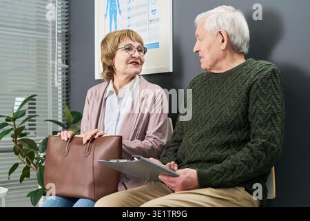 Eine ältere Frau, die mit einem älteren Mann im Wartezimmer der Klinik spricht Stockfoto