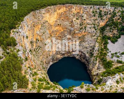 Aus der Vogelperspektive auf das dramatische dunkle Wasser des Roten Sees, das sich in starkem Kontrast zu den steilen, zerklüfteten Klippen und grünen Waldrändern befindet, Imotski, Splitsko-dalmati Stockfoto