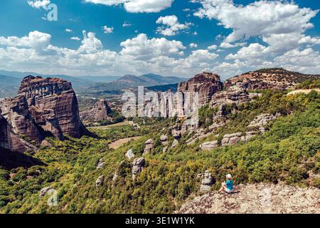 Blick auf hoch aufragende Felsformationen, die die Skyline durchdringen, üppiges Grün über das Gelände, eine Einzelfigur, die die Landschaft betrachtet, Kalabaka, Trikala, Stockfoto