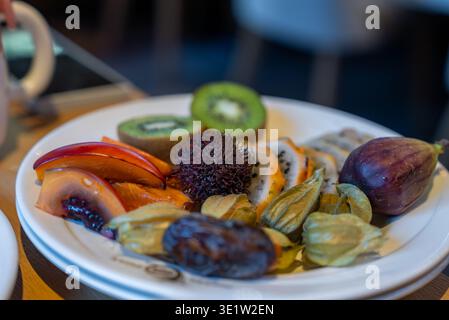 Exotisches Obst auf weißem Teller im dezent beleuchteten Speisesaal Stockfoto