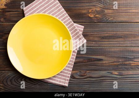 Draufsicht auf farbigem Hintergrund leere runde gelbe Platte auf Tischdecke für Lebensmittel. Leeres Gericht auf Serviette mit Platz für Ihr Design. Stockfoto