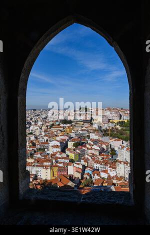 Ein antiker Steinbogen umrahmt einen hohen Blick auf die farbenfrohen, pastellfarbenen Gebäude und Terrakotta-Dächer des alten Lissabon, Portugal. Stockfoto