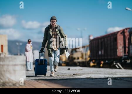 Junge Touristen, die mit einem blauen Koffer und einer Papierkarte durch einen Bahnhofbahnhof laufen Stockfoto
