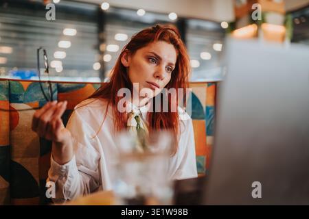 Büroangestellte schaut in einem Café auf den Laptop, während sie ferngesteuert arbeiten und eine Brille halten Stockfoto