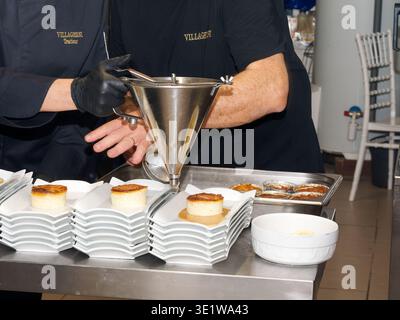 Kochen Sie Desserts mit einem Trichterspender in einer professionellen Küche und ordnen Sie Portionen auf mehreren Tellern an. Szene hebt kulinarische Präzision hervor A Stockfoto