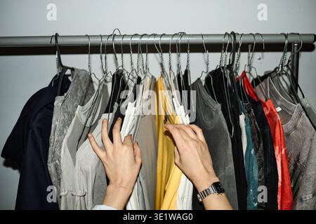 Junge erwachsene Frau, die im Kleiderständer drinnen hängende Hemden durchsucht Stockfoto