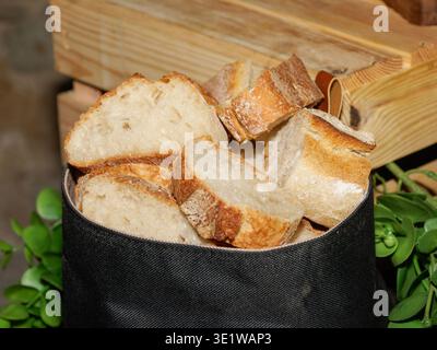 Nahaufnahme von rustikalem, handwerklichem Brot, in Stücke geschnitten und in einen Behälter mit hölzernem Hintergrund gelegt. Frisches knuspriges Brot mit weicher Innenausstattung, ideal Stockfoto